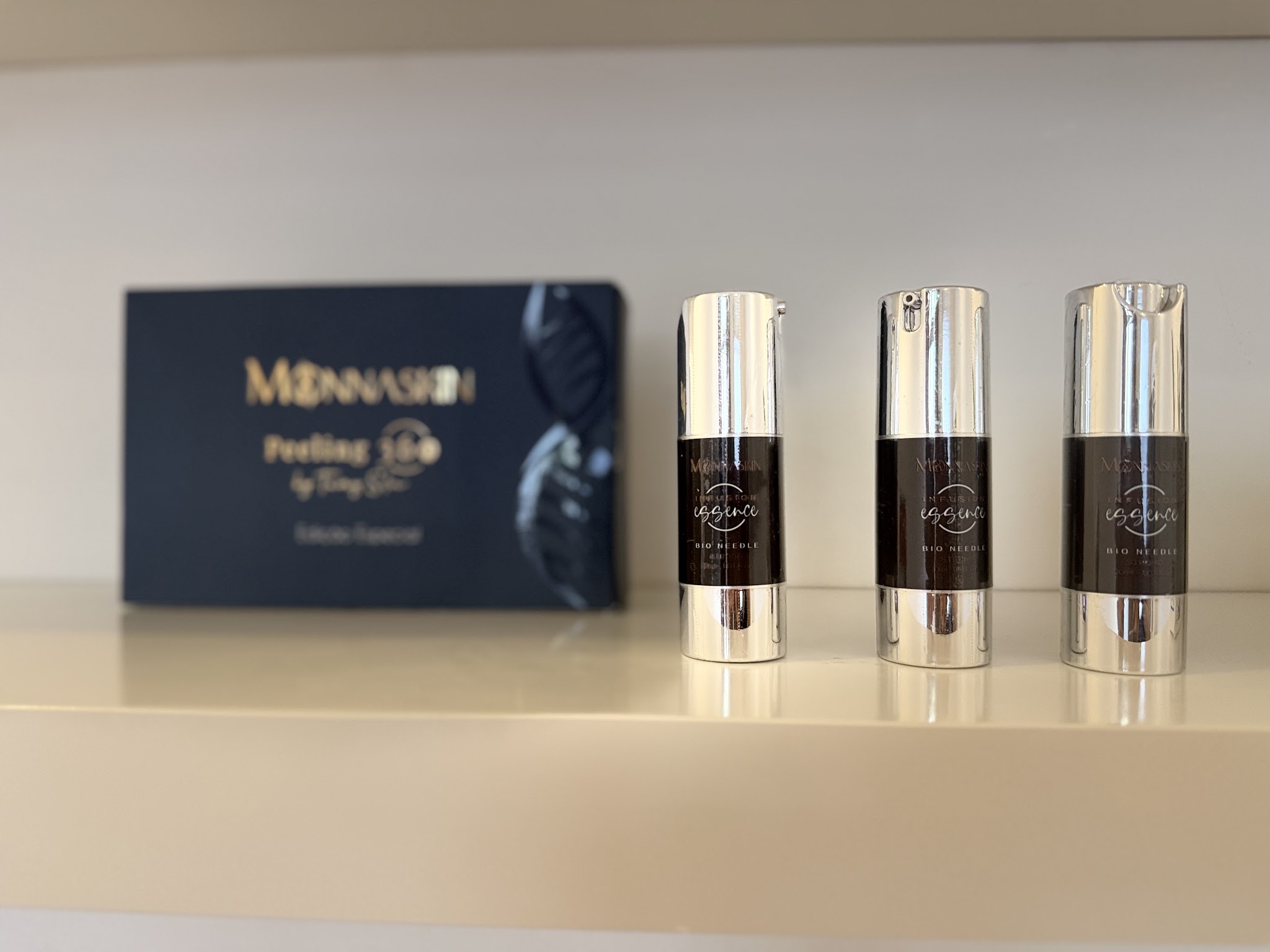 Monnaskin Peeling en drie serumflacons op een witte plank in de studio